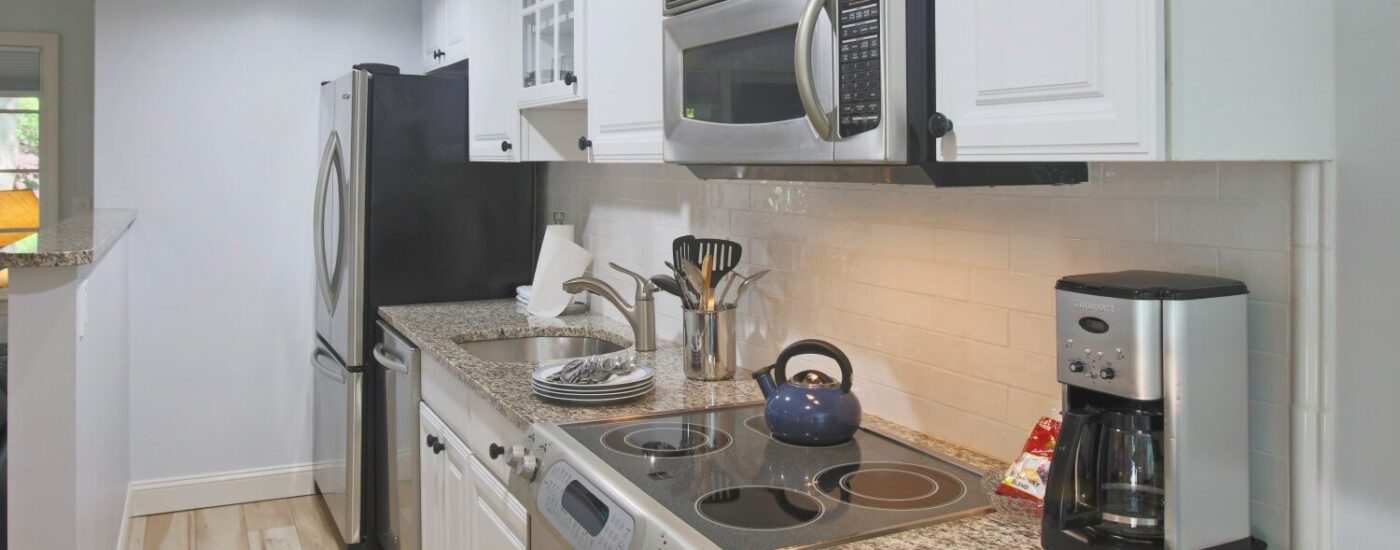 Stainless steel galley kitchen with granite countertop, and white cabinets.